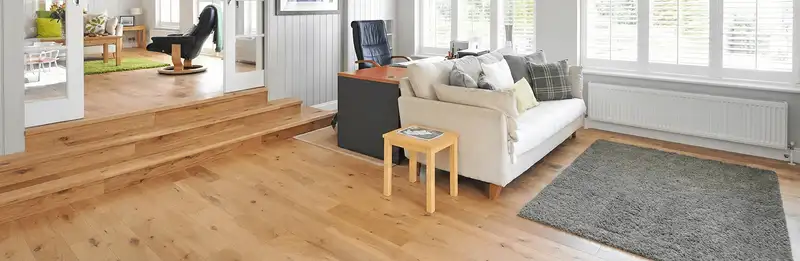 A modern living room with professionally installed laminate flooring, a beige sofa, a small side table, a gray rug, and large windows with white shutters in St Paul, MN